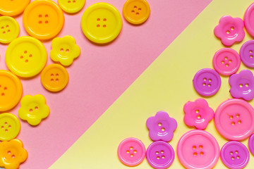 Various pink and yellow sewing buttons on light yellow and pink background with place for text