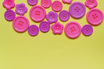 Fototapeta na wymiar Various pink sewing buttons on light yellow background