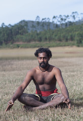 Indian man meditating in lotus yoga pose outdoors in Kerala, South India