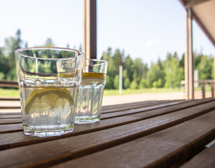 Wooden country furniture on the terrace of a country house. Two refreshing drinks with refreshing lemonade with lemon slices in the foreground. Lush green foliage