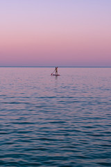 Fototapeta premium Seascape view of a silhouette of a wooman on a paddle board on calm sea water during a beautiful sunset in summer, Vis island, travel Croatia