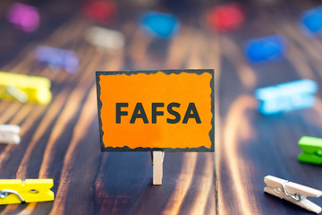 sign board with an inscription FAFSA, Free Application for Federal Student Aid, on a wooden background and colored clothespins