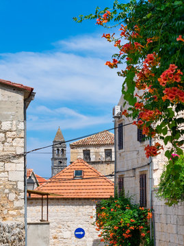Fototapeta Typical scene from a mediterranean village with stone houses, red rooftops, a church tower, and overgrown with vegetation and flowers in summer, Vis island, travel Croatia