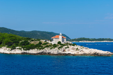 Fototapeta na wymiar Seascape view of a small lighthouse on a green peninsula at the entrance of city of Vis harbour in Croatia, on a bright summer day