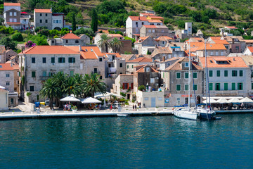 Fototapeta na wymiar Old city of Vis viewed from the sea entering the harbor with old stone houses with red rooftops and sailing boats anchored in summer, Vis island, Croatia