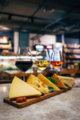 Glasses of Wine and cheese. Assortment or various type of cheese and wine glasses on the table in restaurant. Red, rose and yellow wine or champagne on the table. Winery concept image