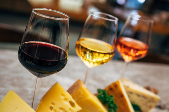 Glasses of Wine and cheese. Assortment or various type of cheese and wine glasses on the table in restaurant. Red, rose and yellow wine or champagne on the table. Winery concept image