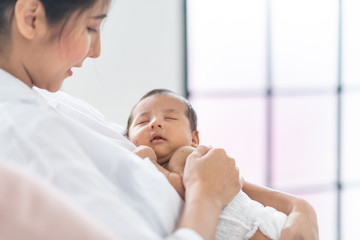 Portrait of beautiful mother playing with her 1 months old baby in the bed