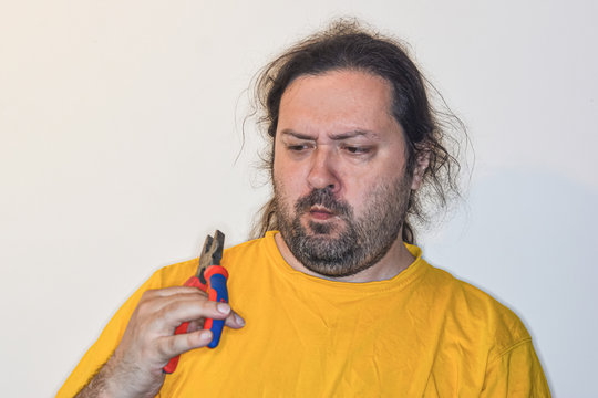 A middle aged man looks at pliers with great astonishment.