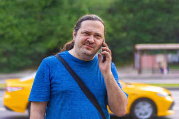 Unshaven middle-aged man talking displeasedly on the phone against the background of a car in a...