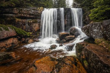 Amazing waterfall in the middle of mountain forest. River full of water during spring, beautiful flowing mass. Lovely contrast of water and surrounding forest green. Stones and fresh green leaves.