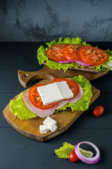 Breakfast tomato sandwich with salad on black wood background.