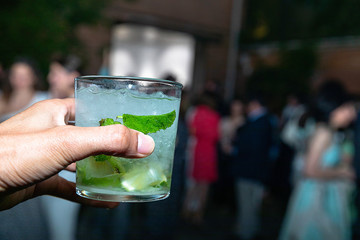 Hand celebrating a toast with a mojito with lemon, mint and ice at a party