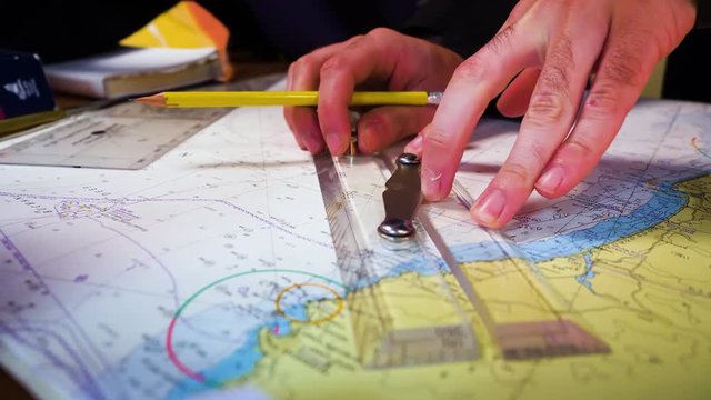 Yachts navigator using a parallel ruler and pencil while plotting a course on a chart at sea