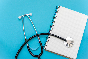 Medical stethoscope and blank notebook isolated on blue background top view. Treatment and health care concept.