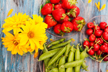 Summer composition on the table: yellow flowers, strawberries, cherries and peas