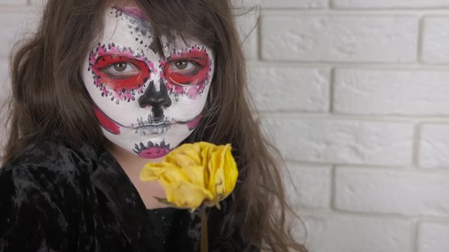 Little girl with a rose on the day of the dead. Sad little girl in costume and dead rose for halloween.