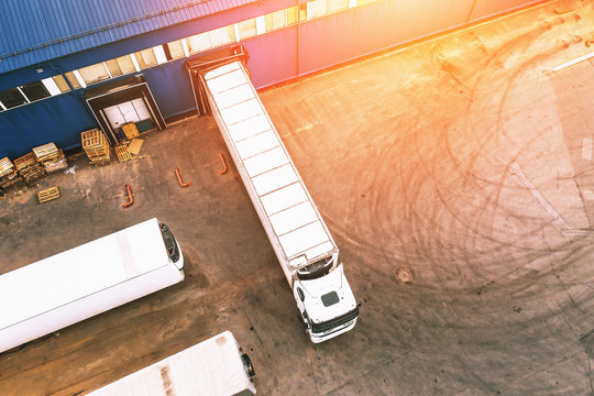 Aerial photo of cargo trucks in industrial warehouse or logistic center waiting for loading goods in sunset light, top view