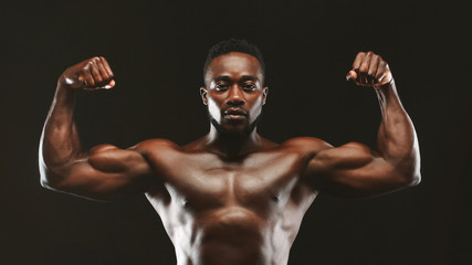 Obraz premium Black athlete flexing muscles, demonstrating strong biceps