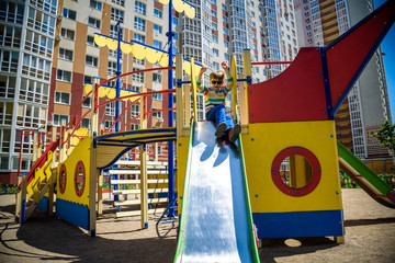 summer, childhood, leisure, friendship and people concept - happy little boy on children playground slid from the hill