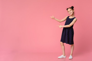 Cheerful girl in stylish dress pointing at empty space