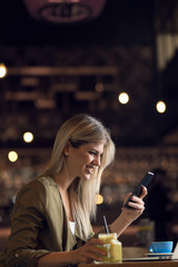 Happy young woman reading something from her mobile phone in a cafe