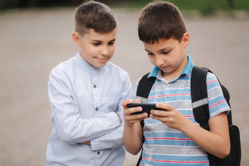 Two boy sitting on the bench and play online games. One boys with backpack. Young boys use their phones