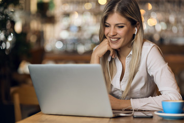 Happy young woman listening music over her laptop  in a cafe