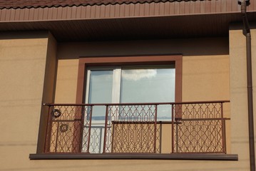 one open metal balcony with a glass door and a window on the brown wall of the house