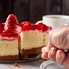 Hand lifted up piece of cheesecake with strawberries