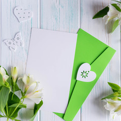 Mock up blank paper and envelope on white wooden background with natural flowers of white color. Blank, frame for text. Greeting card design with flowers. Aalstroemeria on wooden background.