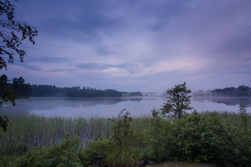 Gorgeous view of fog on the lake in the evening time on summer day. White clouds on blue sky. Europe. Sweden. Gorgeous backgrounds.