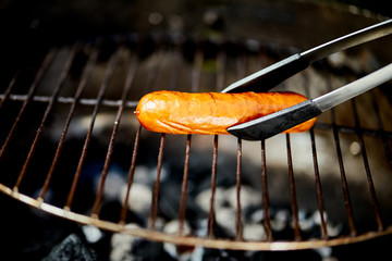 Juicy sausage on hot grill with tongs during summer barbecue