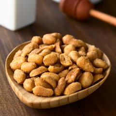 Peanuts with honey and salt in small wooden plate, photographed on dark wood with natural light (Selective Focus, Focus in the middle of the peanuts)