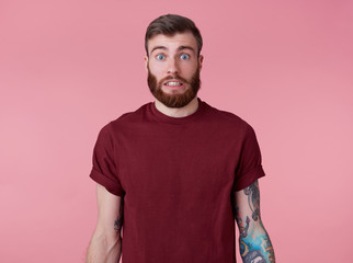 Something wrong! Young attractive tattooed red bearded man in blank t-shirt, looks shocked and sad,...