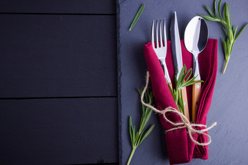 Set of cutlery knife, spoon, fork on slate stone. Сutlery with burgundy napkin and twine. Rosemary...