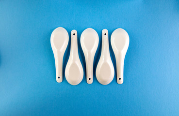 White Asian style spoons arranged in geometric pattern on blue background