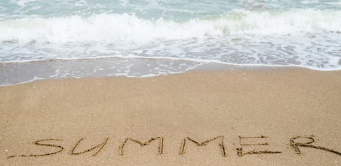 The word Summer written on the beach, the ocean on the sand.