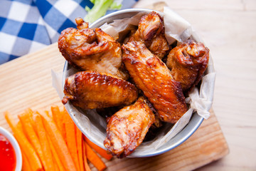 Baked chicken wings with sesame seeds and sweet chili sauce on white wooden board.