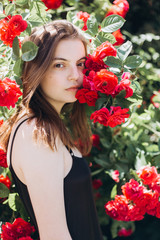 Close up summer portrait of young sensual interesting pretty young woman outdoors near red roses. Modeling, fashion, trends, nature concept