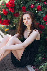 Close up summer portrait of young sensual interesting pretty young woman outdoors near red roses. Modeling, fashion, trends, nature concept