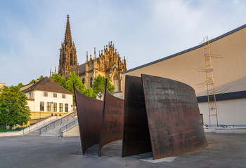 Outdoor sunny view at rusty metal sculpture art installed on plaza near Carnival Fountain, and background of Offene Kirche Elisabethen, Grand neo-gothic churc, in city center of Basel, Switzerland. - obrazy, fototapety, plakaty