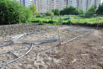 installation of domed greenhouses on the ground, consisting of steel profiles and plastic. In the background there is a Church, private and multi-storey buildings.