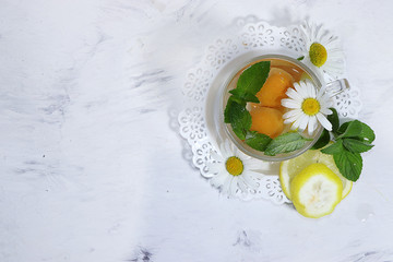 Obraz na płótnie Canvas Herbal tea with mint, chamomile and lemon on a sunny table, top view. Summer drinks made from natural herbs are very useful and energize and have a good mood.