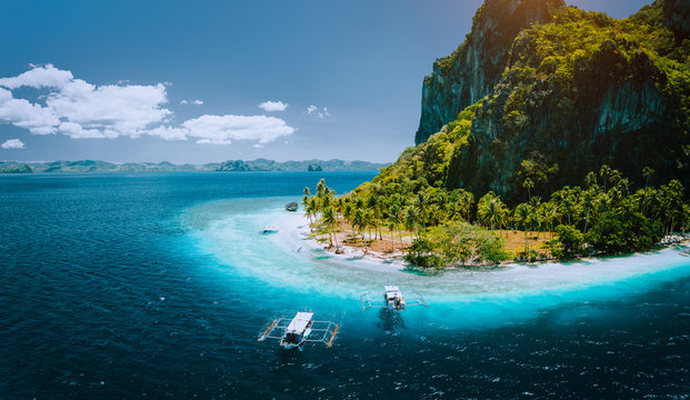 Epic aerial drone panoramic picture of tourist boats arriving tropical Pinagbuyutan Island with idyllic ipil beach surrounded by turquoise blue ocean water. El Nido, Palawan, Philippines