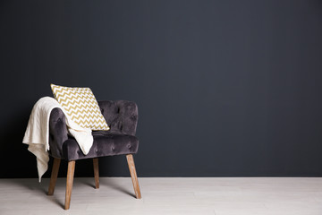 Stylish armchair with pillow and plaid near dark wall, space for text. Interior design