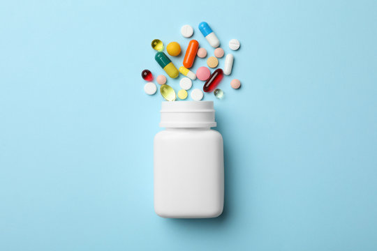 Bottle and scattered pills on color background, top view