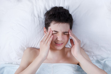 the severe headache, the teenager, the boy keeps hands on the head in a bed