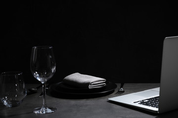 Composition with tableware and laptop on table against black background, space for text. Loneliness...