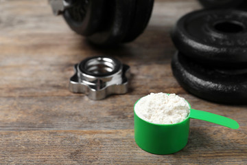 Scoop with protein powder and dumbbell parts on wooden table. Space for text